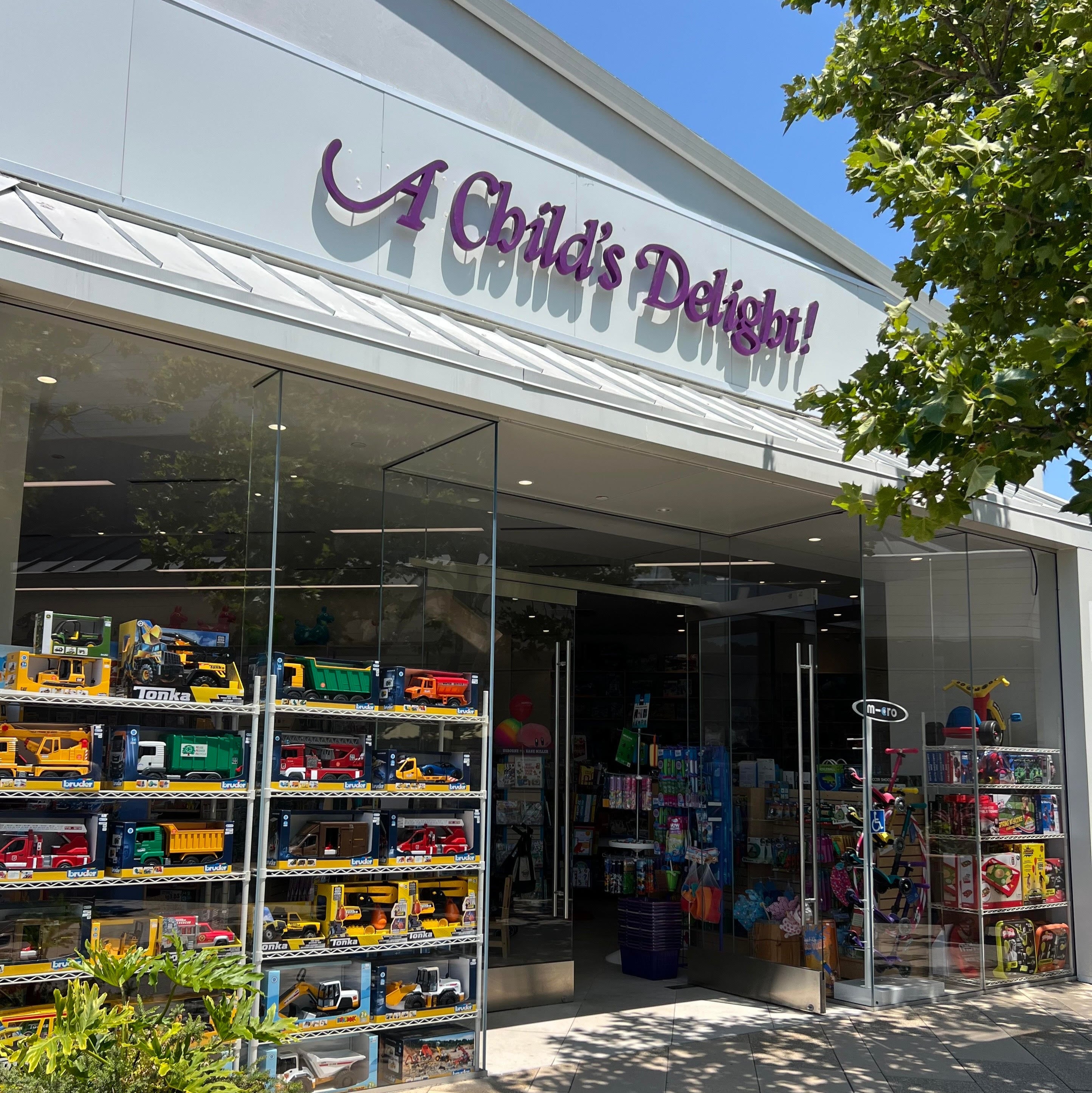 Storefront of 'A Child's Delight' with toy display through glass windows on a sunny day.